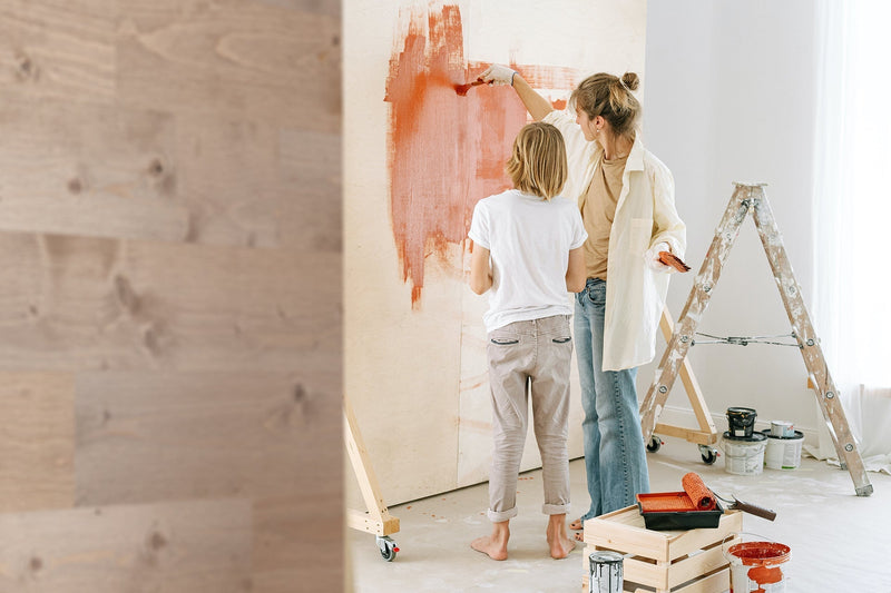 Two people painting a wall beside a pale wood plank accent