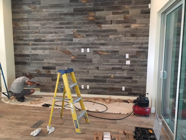 Person installing Stikwood peel-and-stick reclaimed wood planks on an accent wall — no nails or tools required