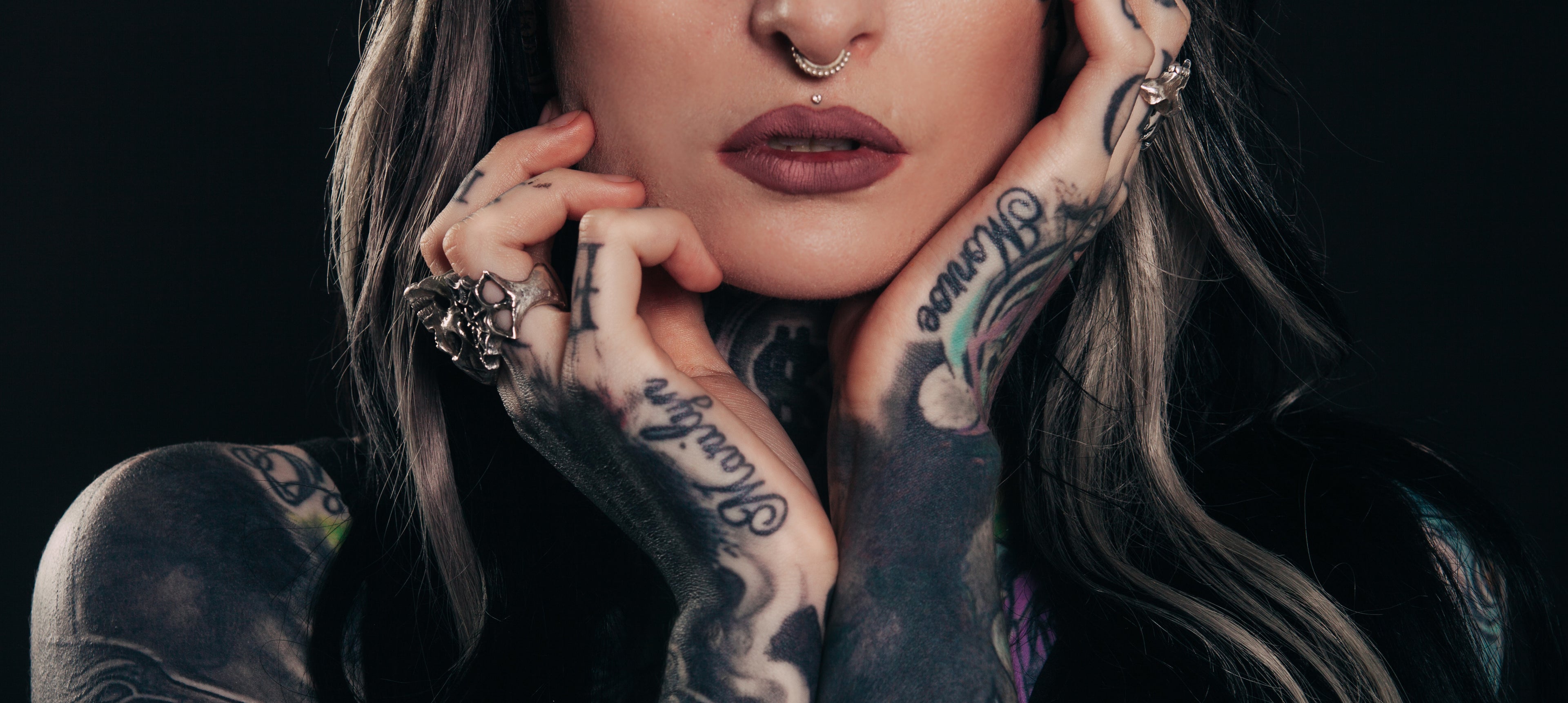 Close up of person with multiple rings and tattoos on hands and fingers against a dark background